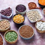 Various grains and legumes, such as lentils, rice, and chickpeas, are arranged in bowls, representing staples of a Mediterranean Diet. 