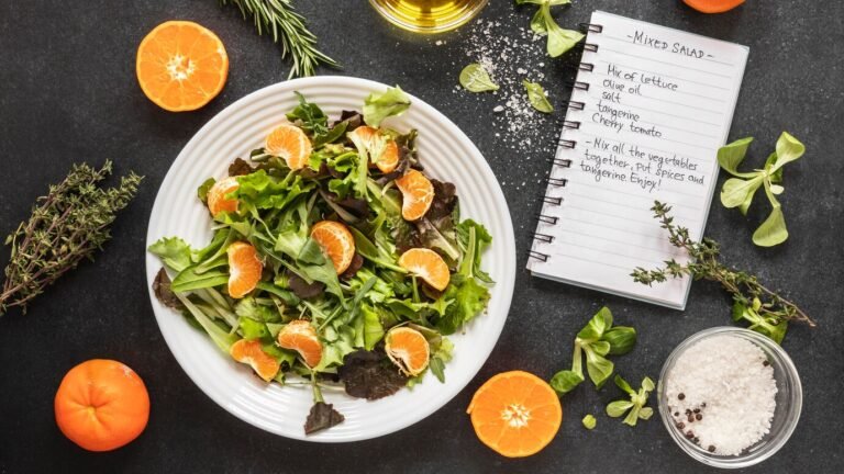 A simple Mediterranean-inspired salad with tangerine segments, mixed greens, and black olives, with a small bowl of salt and peppercorns to the side.