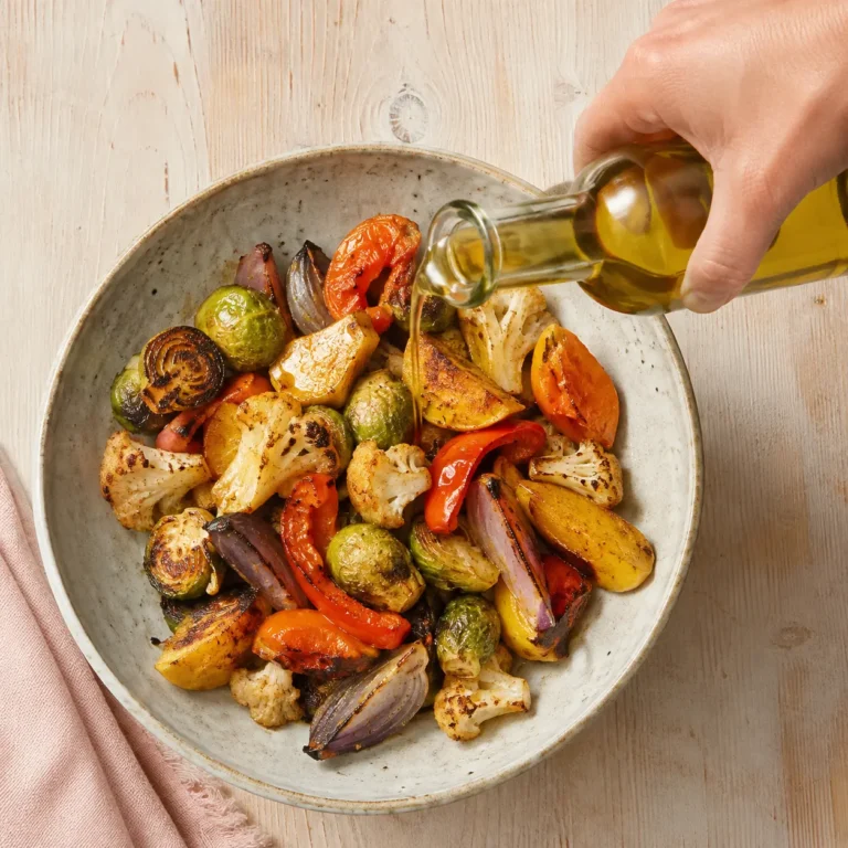 Hand drizzling olive oil over a bowl of roasted vegetables for a PCOS-friendly Mediterranean meal