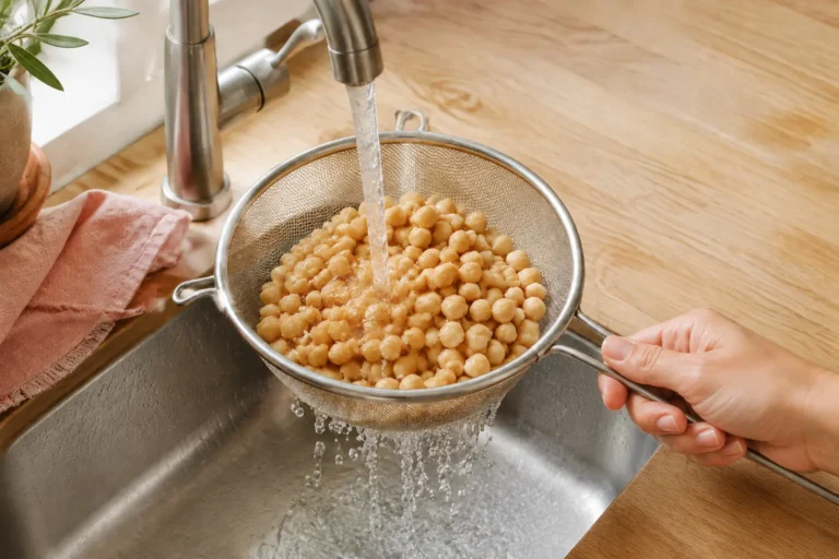 Hand rinsing cooked chickpeas in a metal strainer under running water for a PCOS-friendly meal.